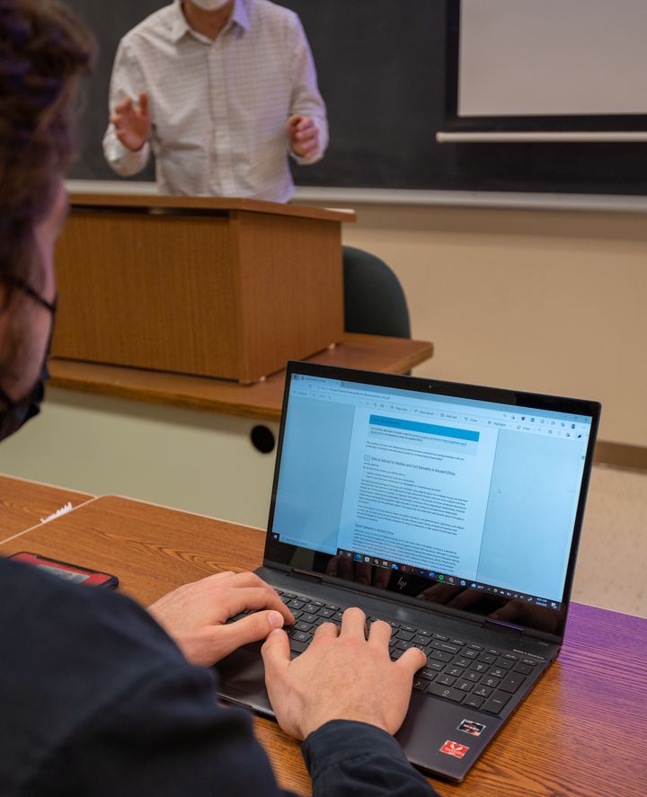 A student looks at an online textbook with his laptop in a classroom.